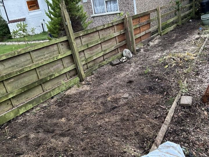 A cleared garden plot with bare soil and wooden fencing in the background.
