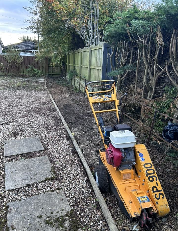 A yellow garden tiller parked beside a gravel path in a garden area.